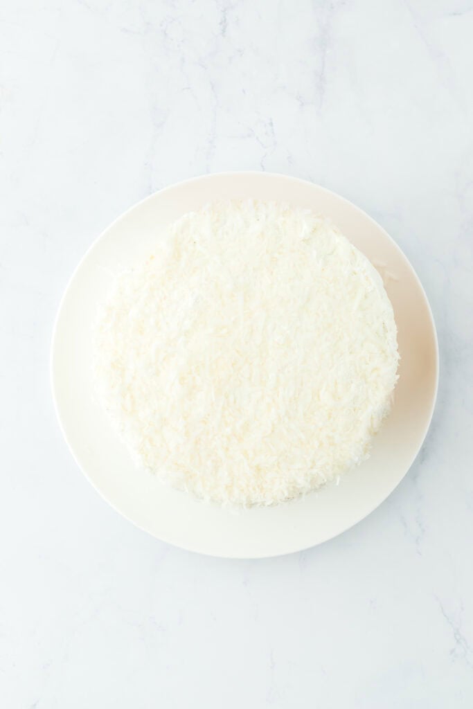 Frosted coconut layer cake on white plate