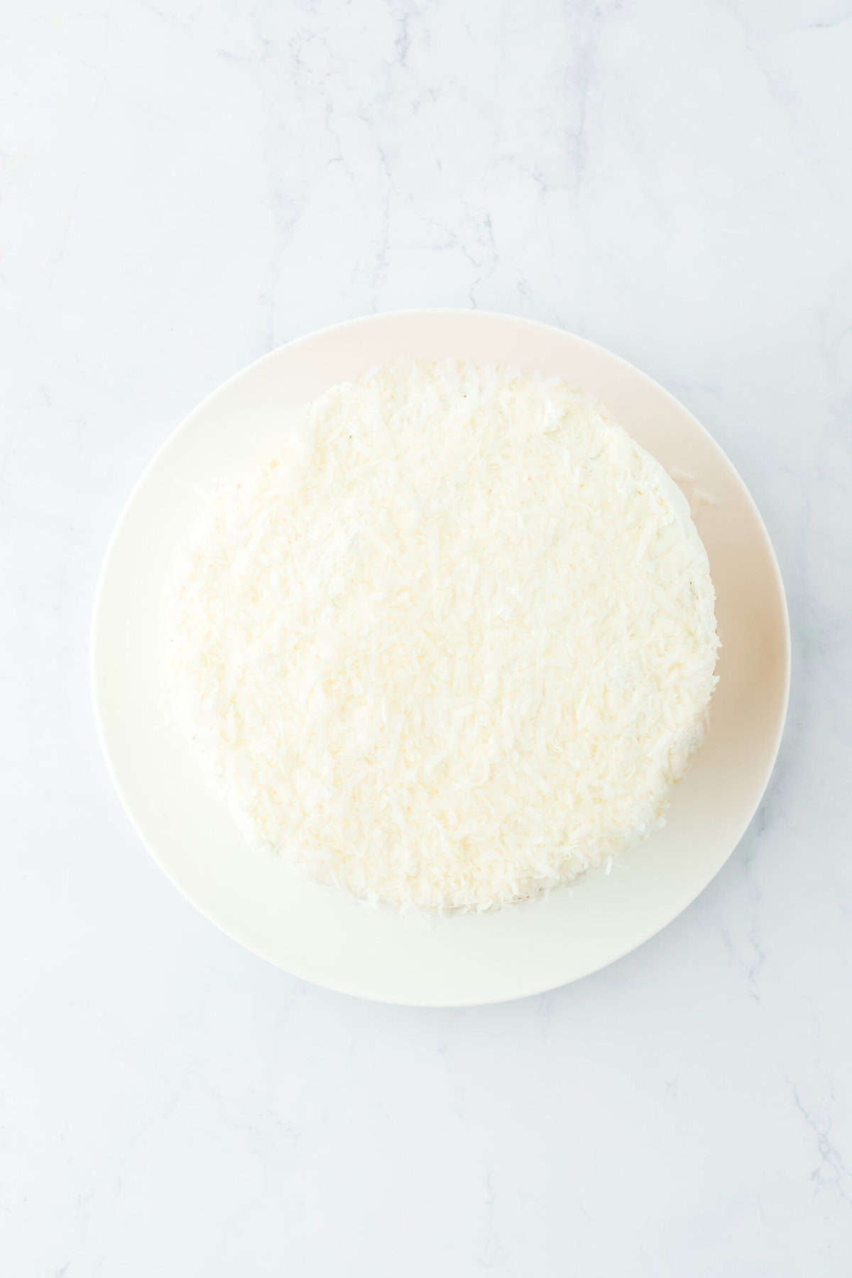 Frosted coconut layer cake on white plate