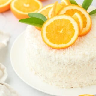 A coconut orange layer cake on a white plate on white countertop