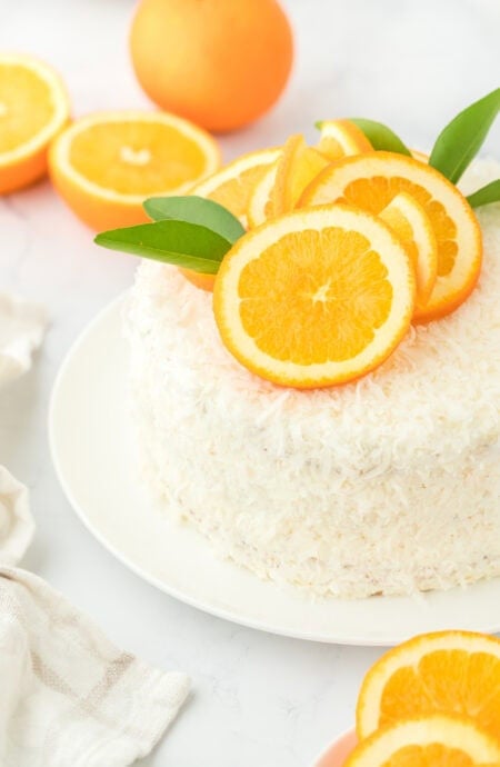 A coconut orange layer cake on a white plate on white countertop