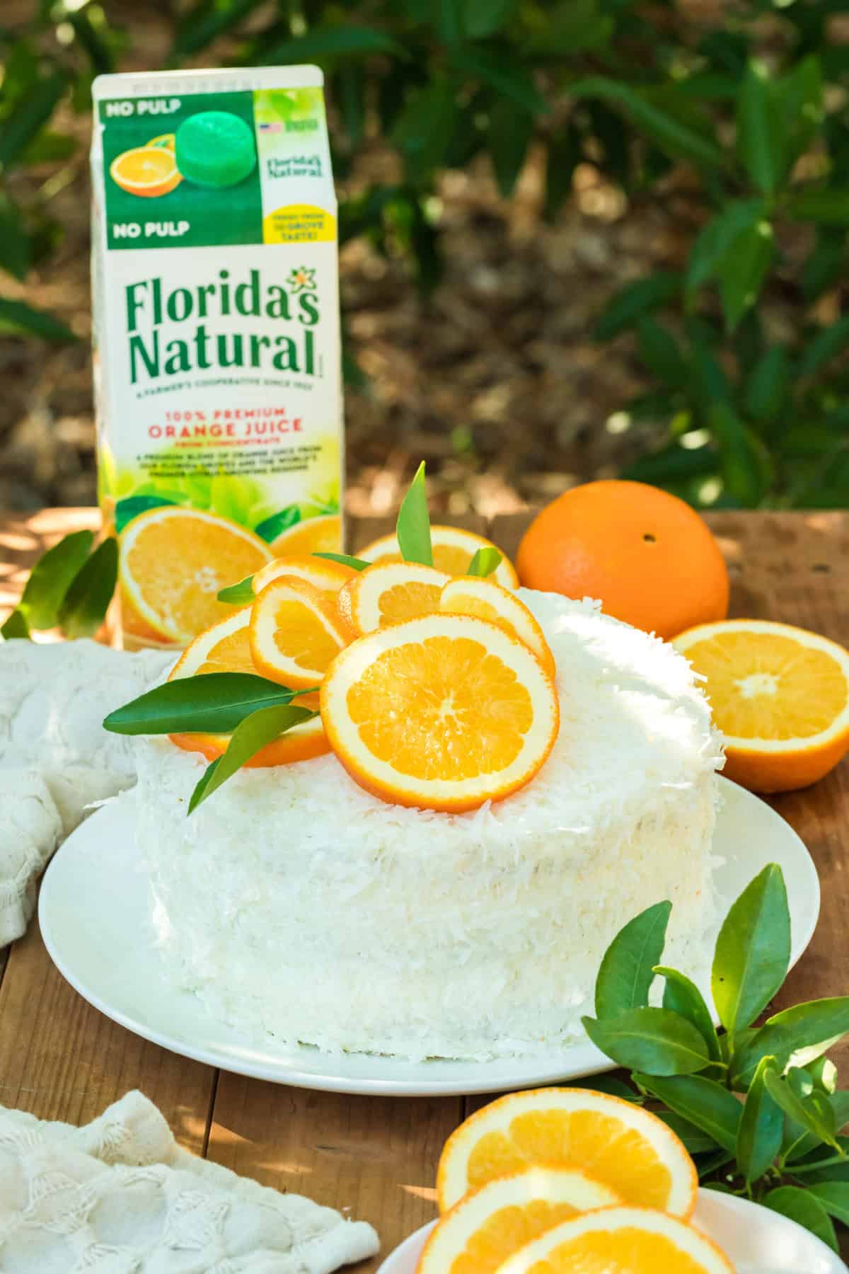 An orange coconut layer cake on a white plate on a wooden table