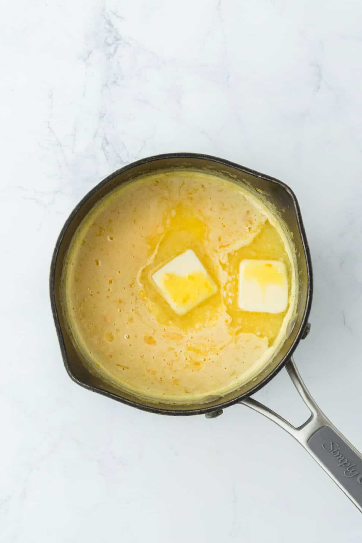 Butter added to an orange curd in a saucepan on white countertop