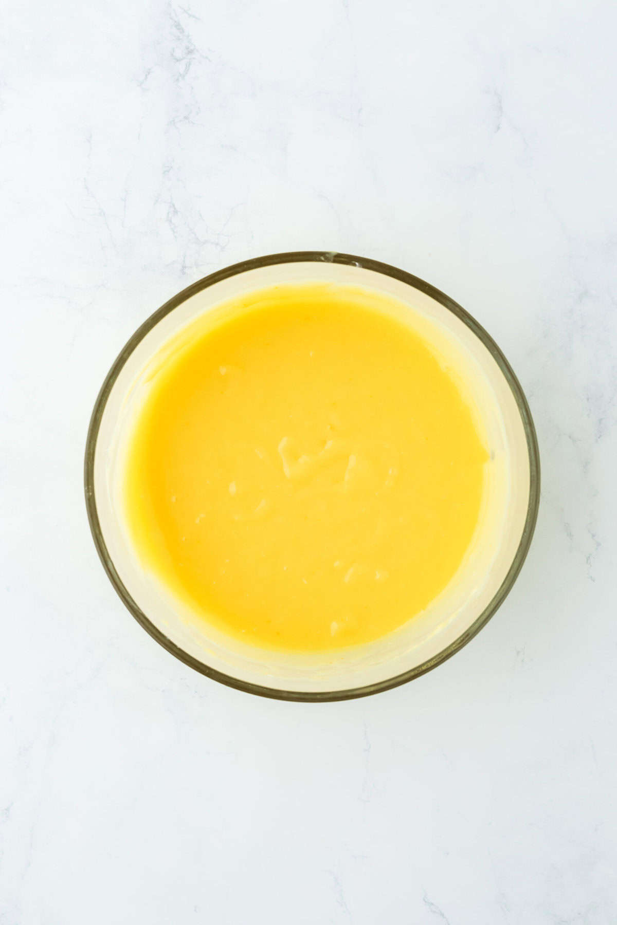 Completed orange curd in a glass bowl on a white countertop