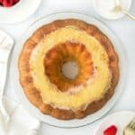 Overhead shot of a whole creme brulee pound cake with raspberries, a small bowl with sugar, and forks in the background