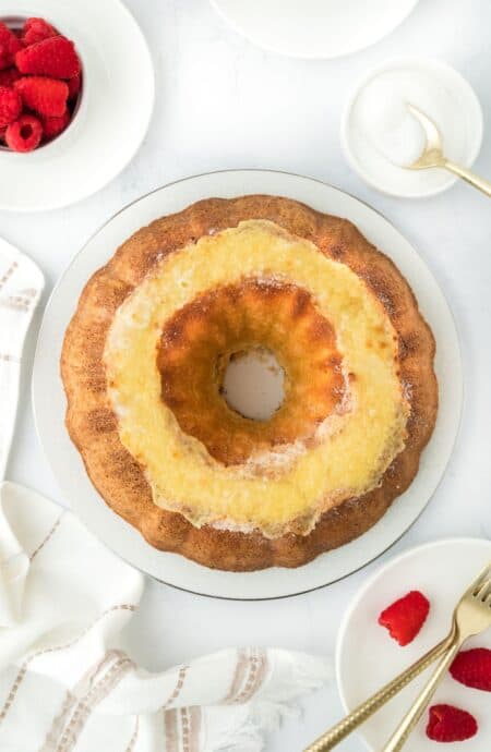 Overhead shot of a whole creme brulee pound cake with raspberries, a small bowl with sugar, and forks in the background