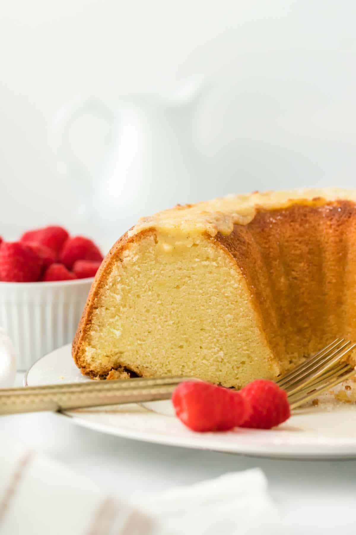 A sliced creme brulee pound cake served on a white plate with vibrant raspberries and a fork, showing the cake's moist texture