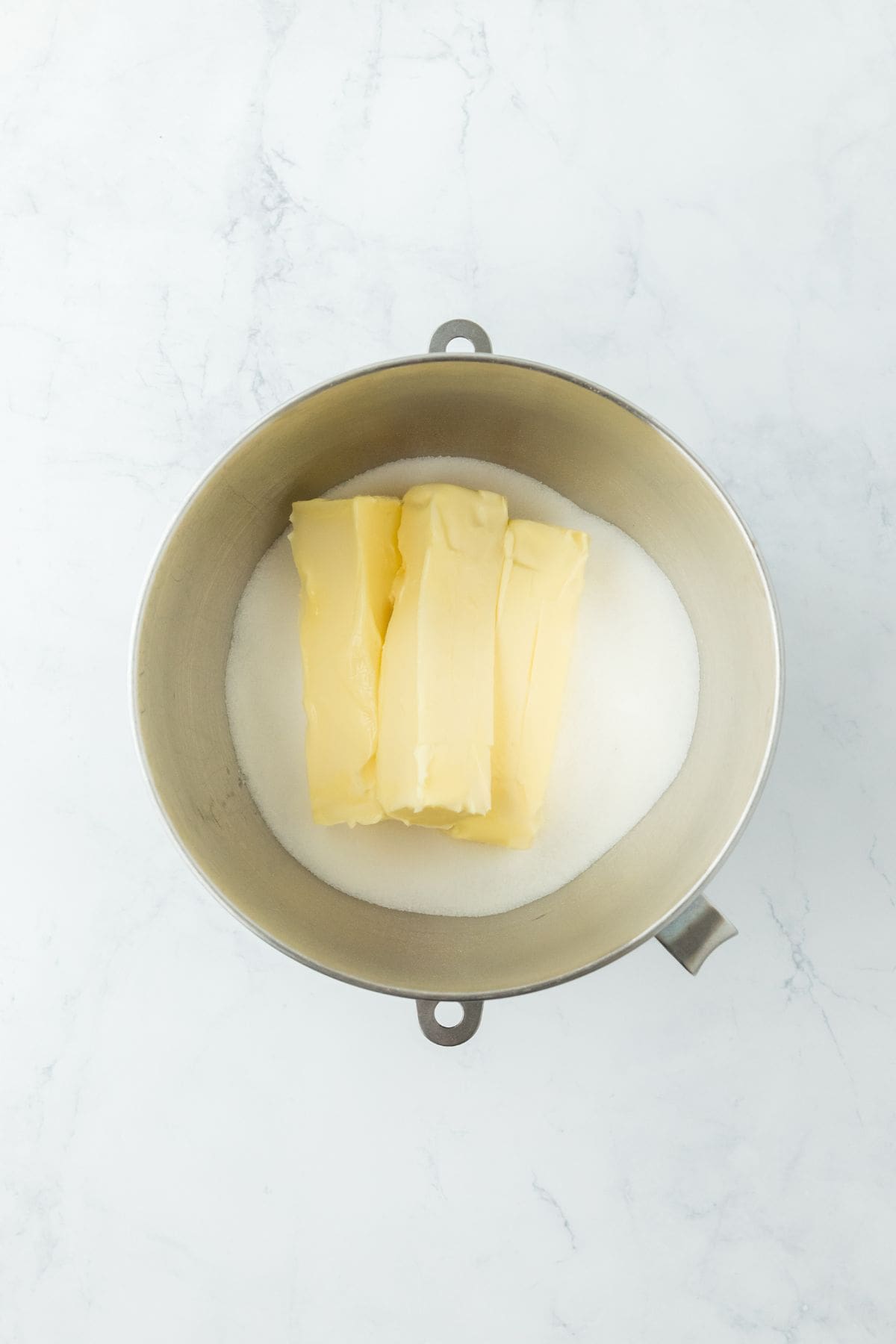 A mixing bowl containing sticks of butter and sugar, prepped for creaming