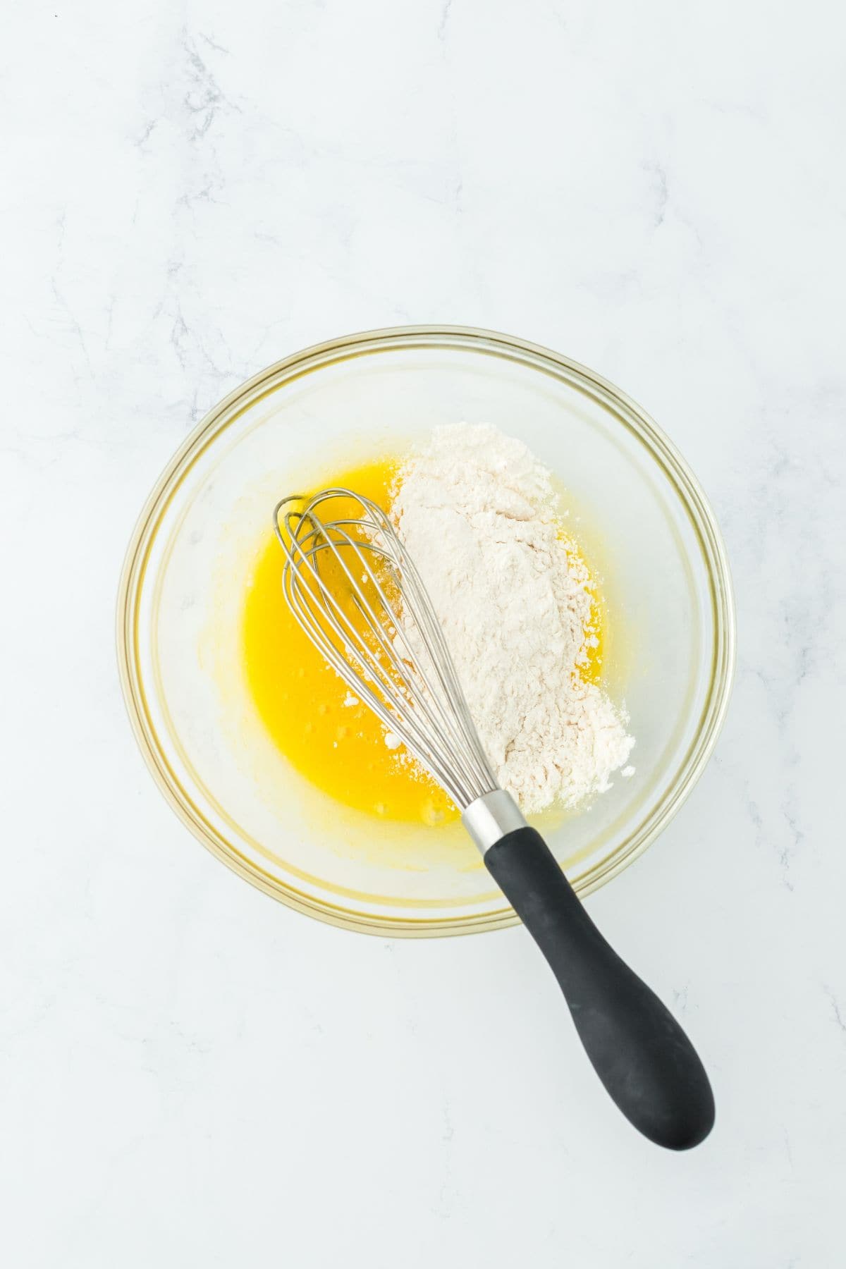 A glass bowl with the egg mixture and flour being added