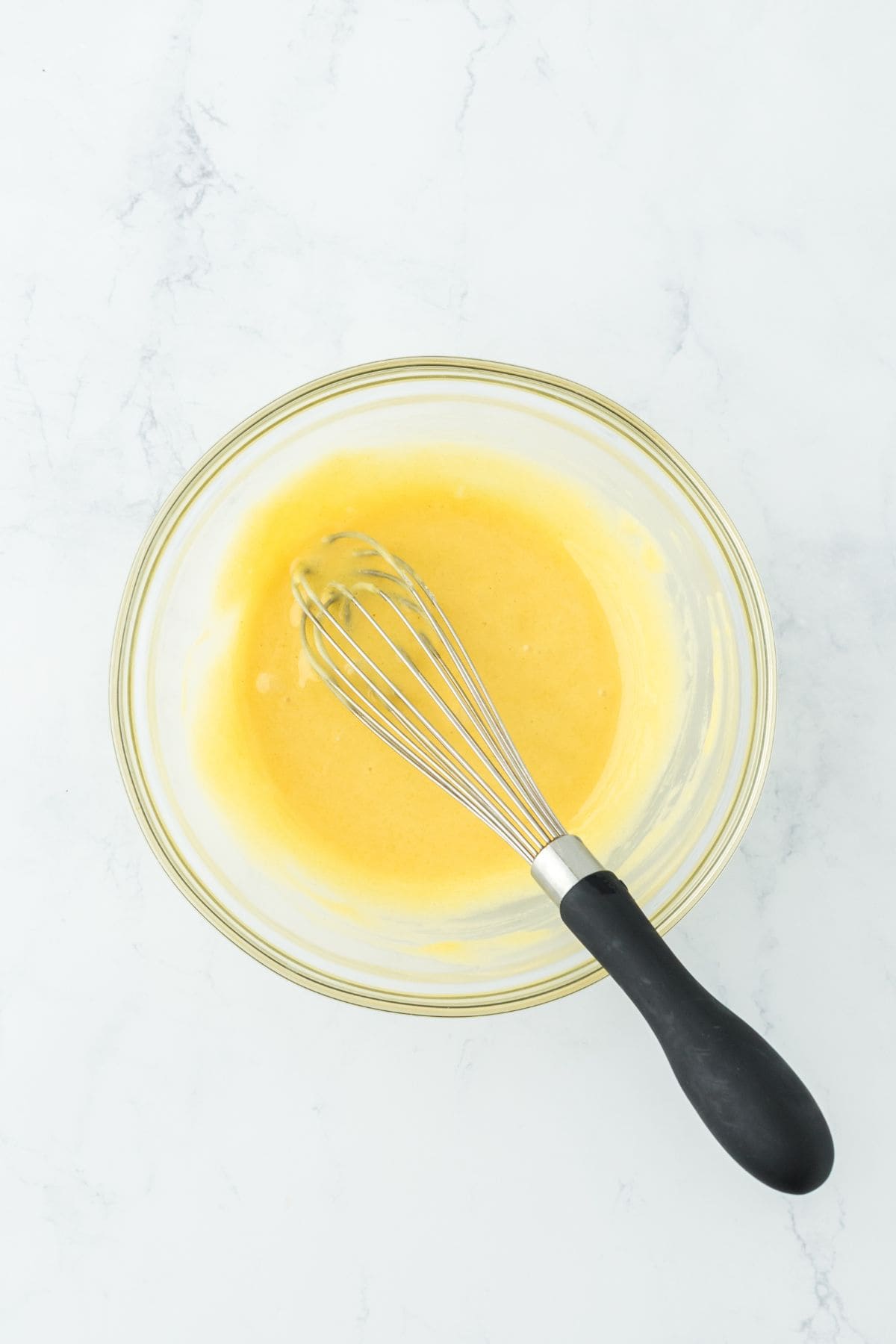 A glass bowl with a smooth yellow batter being whisked to perfection