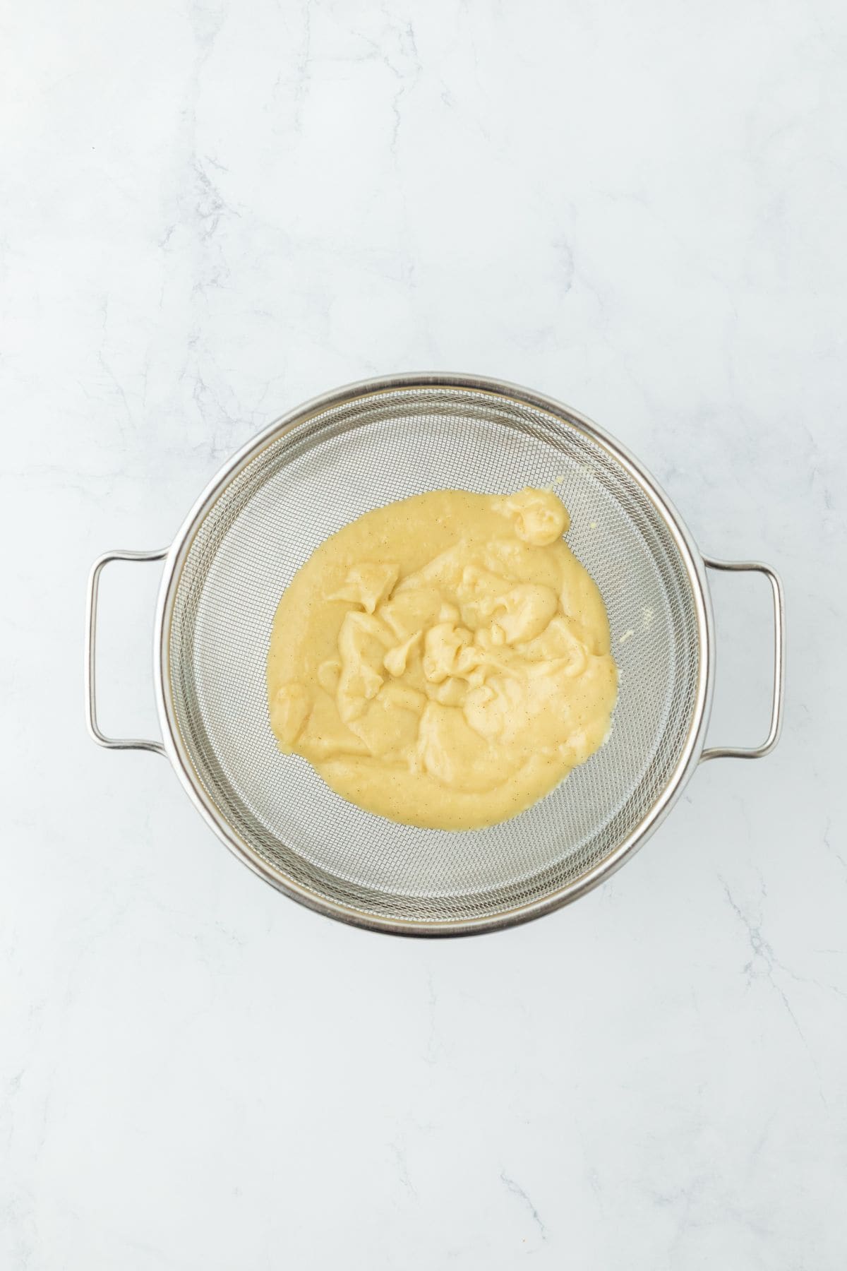 A sieve with creamy custard mixture being strained