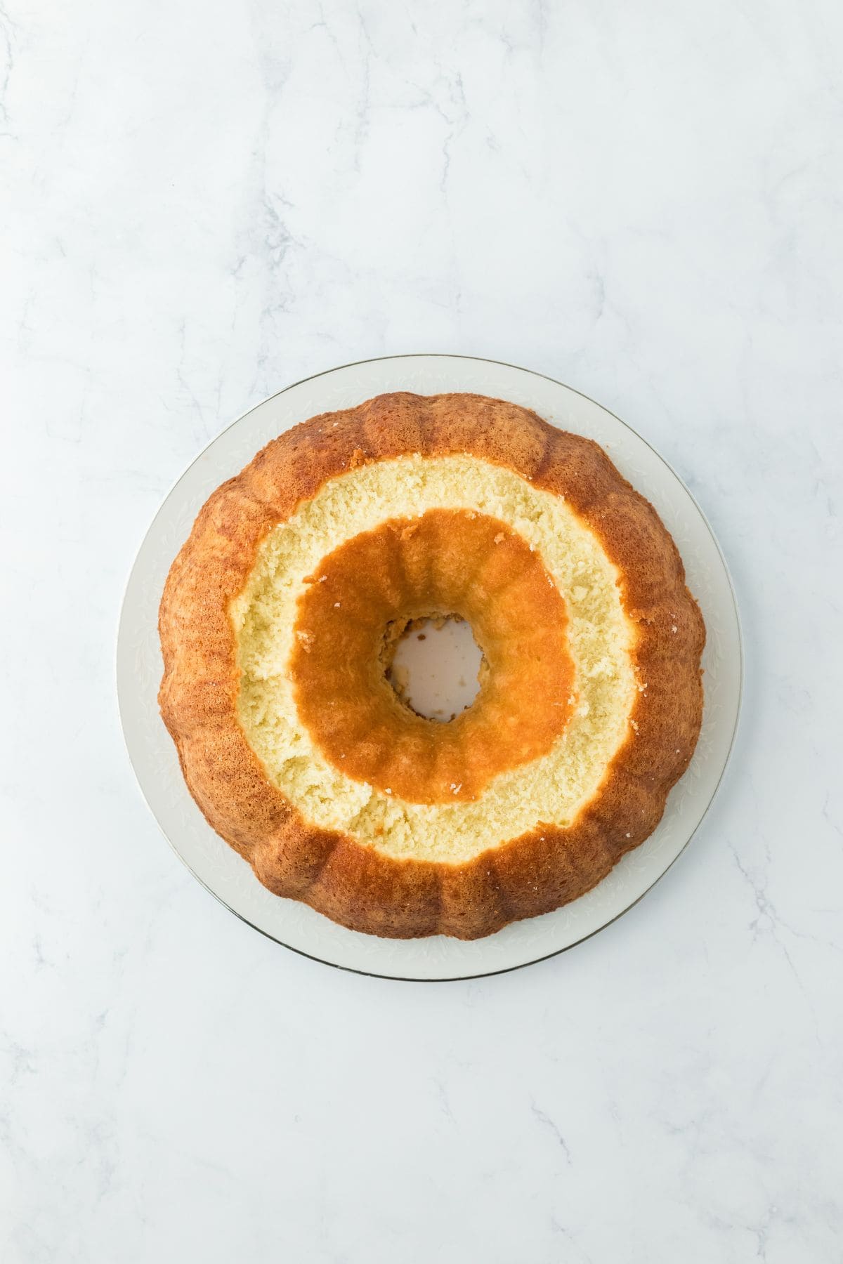 Baked pound cake flipped out of the bundt pan onto a plate, showing a carved ring all around the surface