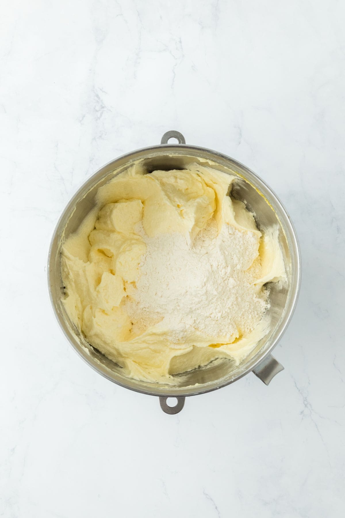 Creamed mixture in a bowl with a portion of dry flour added on top