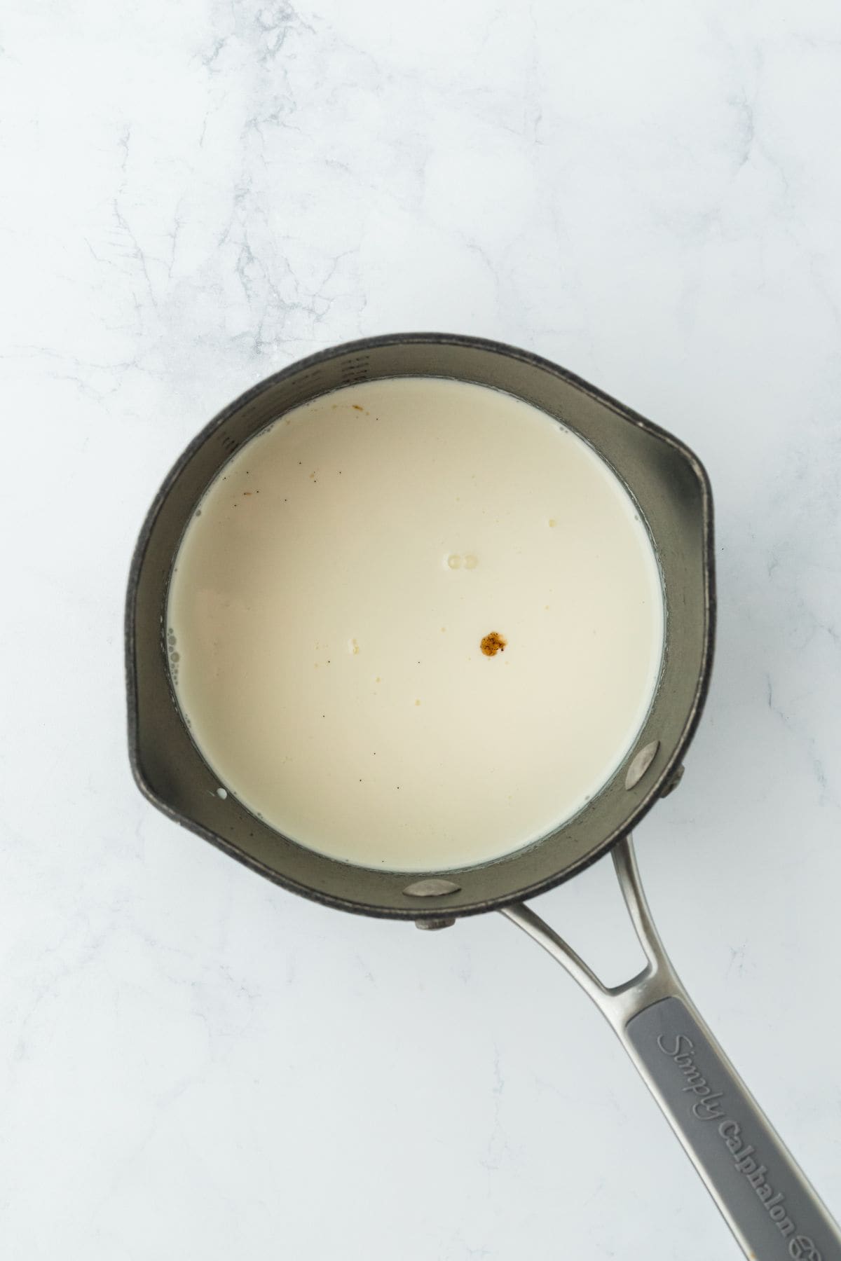 A saucepan filled with cream, showing the first step of heating the mixture with a vanilla speck visible