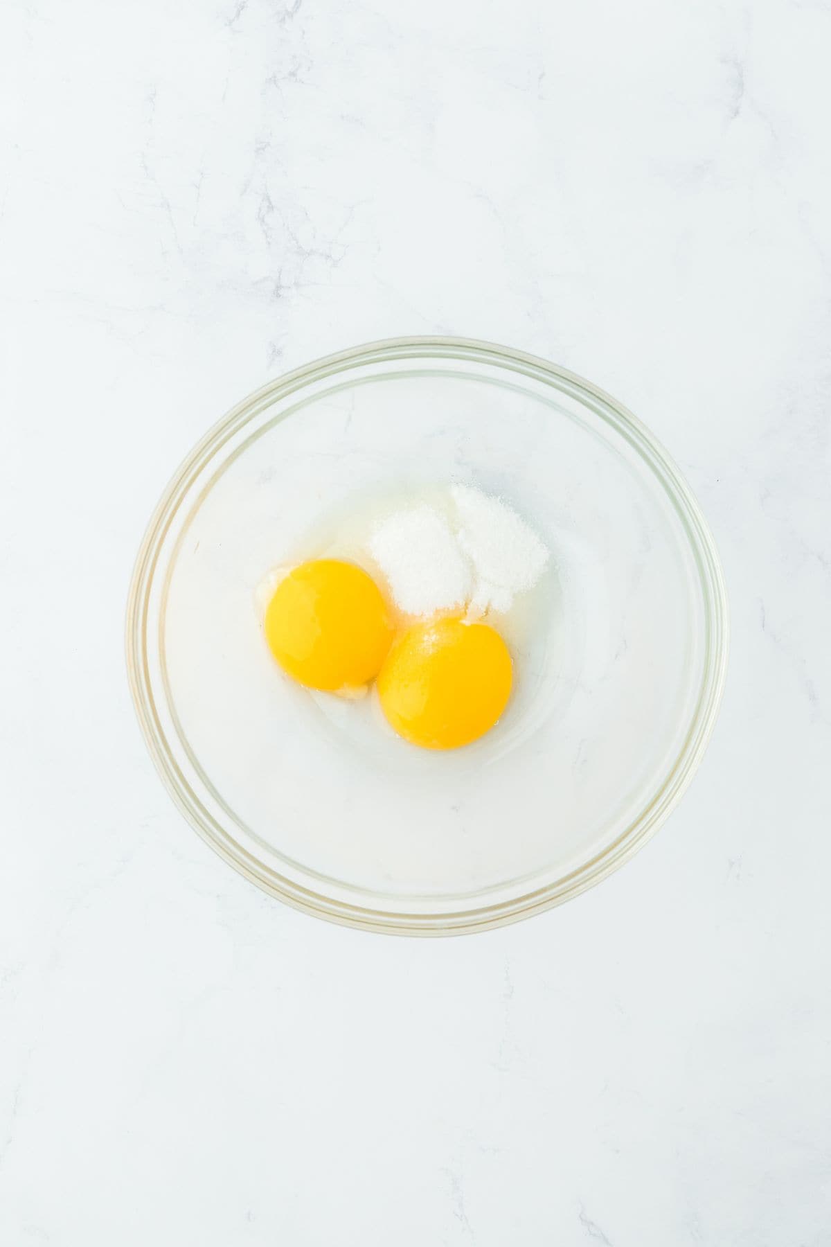 A glass bowl containing two egg yolks and sugar, ready to be whisked together