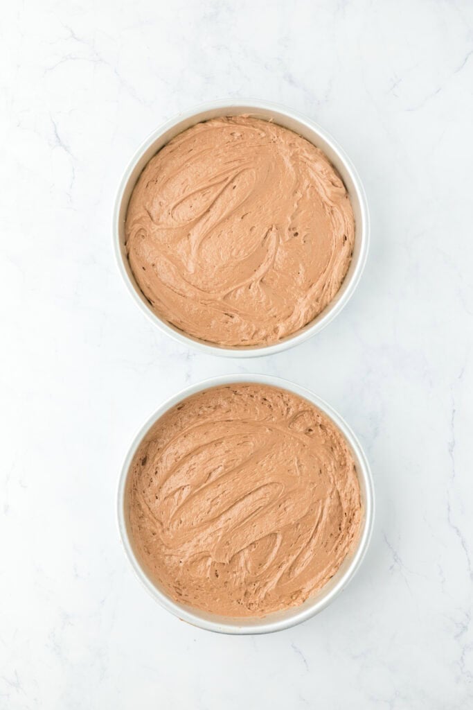 Devil's cake batter added to two cake pans on white countertop.