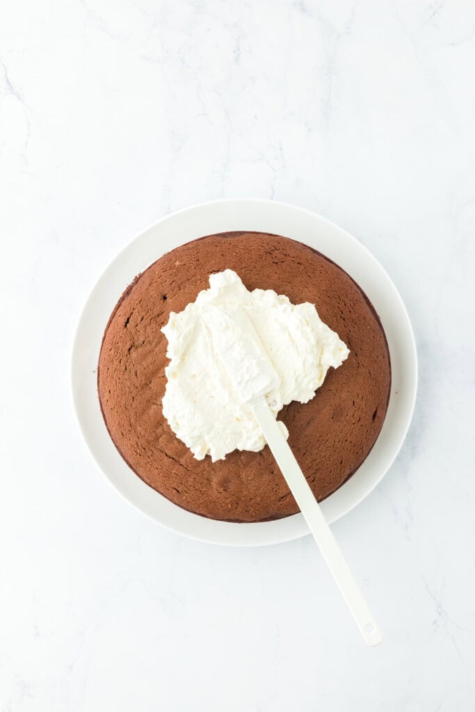 Spread the frosting on chocolate cake on white countertop