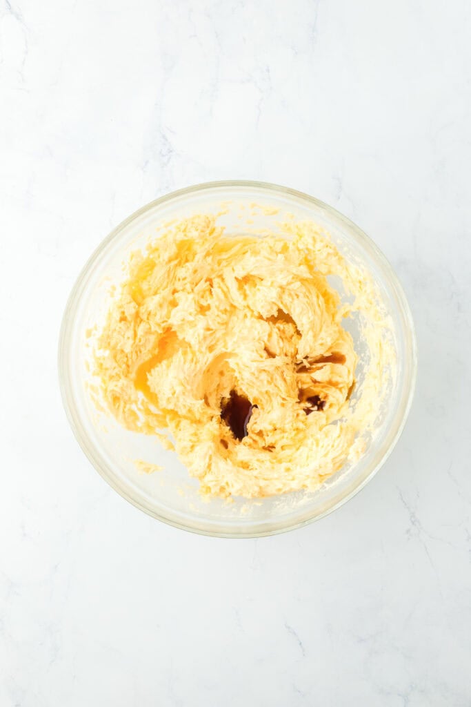Vanilla and oil added to bowl with creamed batter in glass bowl on white countertop