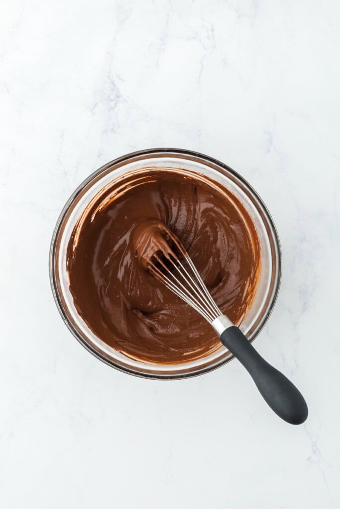 Cocoa powder and hot coffee mixed together in glass bowl on white countertop