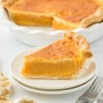 A slice of double crusted sweet potato pie on a small white plate, with the whole pie in the background