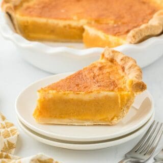 A slice of double crusted sweet potato pie on a small white plate, with the whole pie in the background