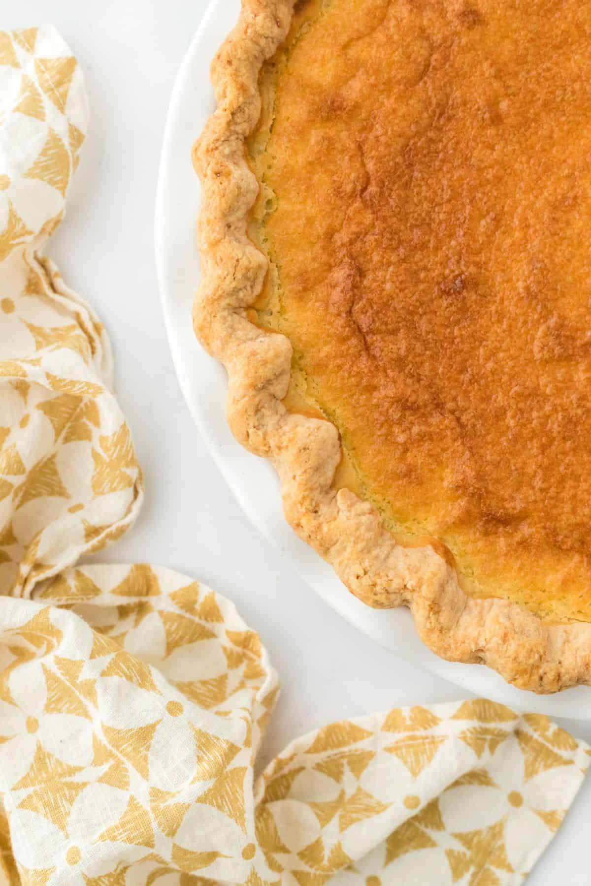 Overhead shot of a golden-brown double crusted sweet potato pie, placed on a white plate with a yellow patterned cloth