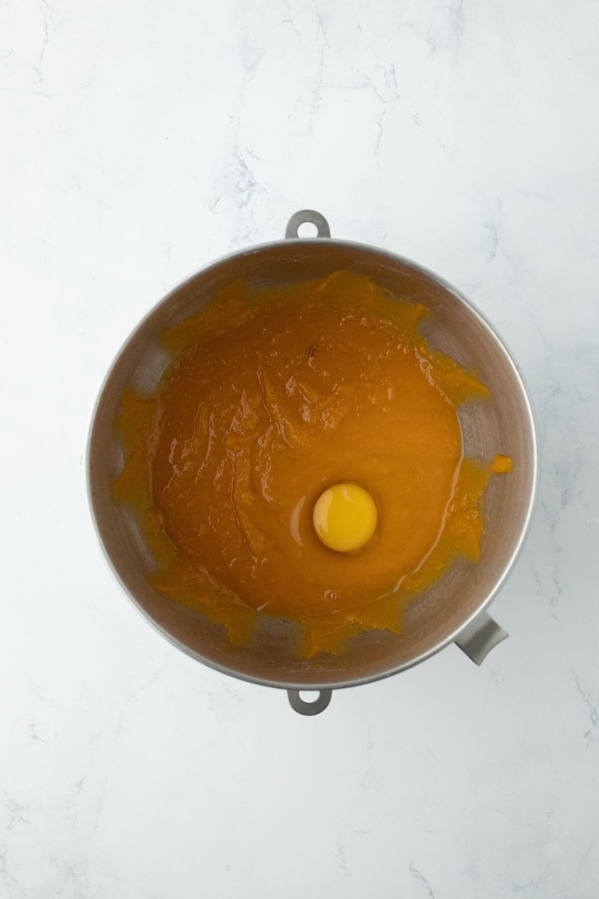 A single egg added to the sweet potato mixture in a mixing bowl