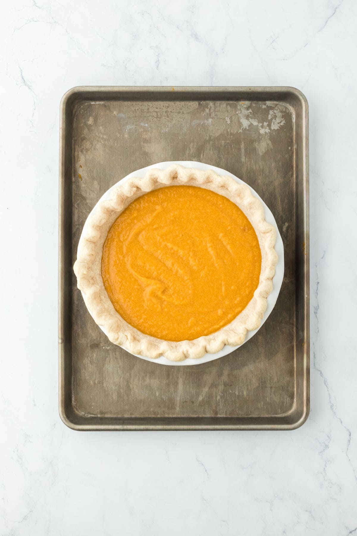 An unbaked pie filled with orange sweet potato filling, set on a baking tray