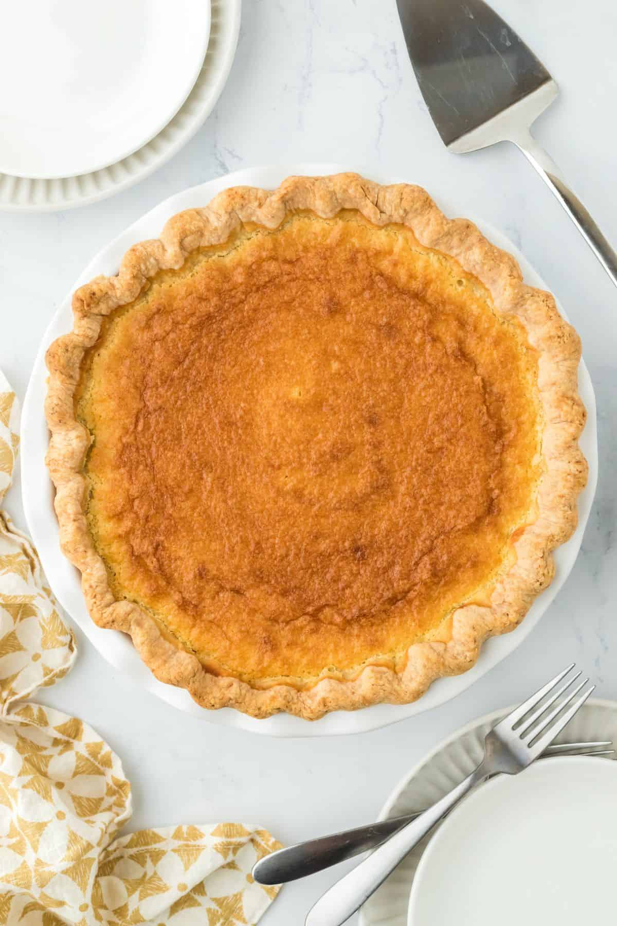 A fully baked double crusted sweet potato pie, surrounded by plates and serving utensils