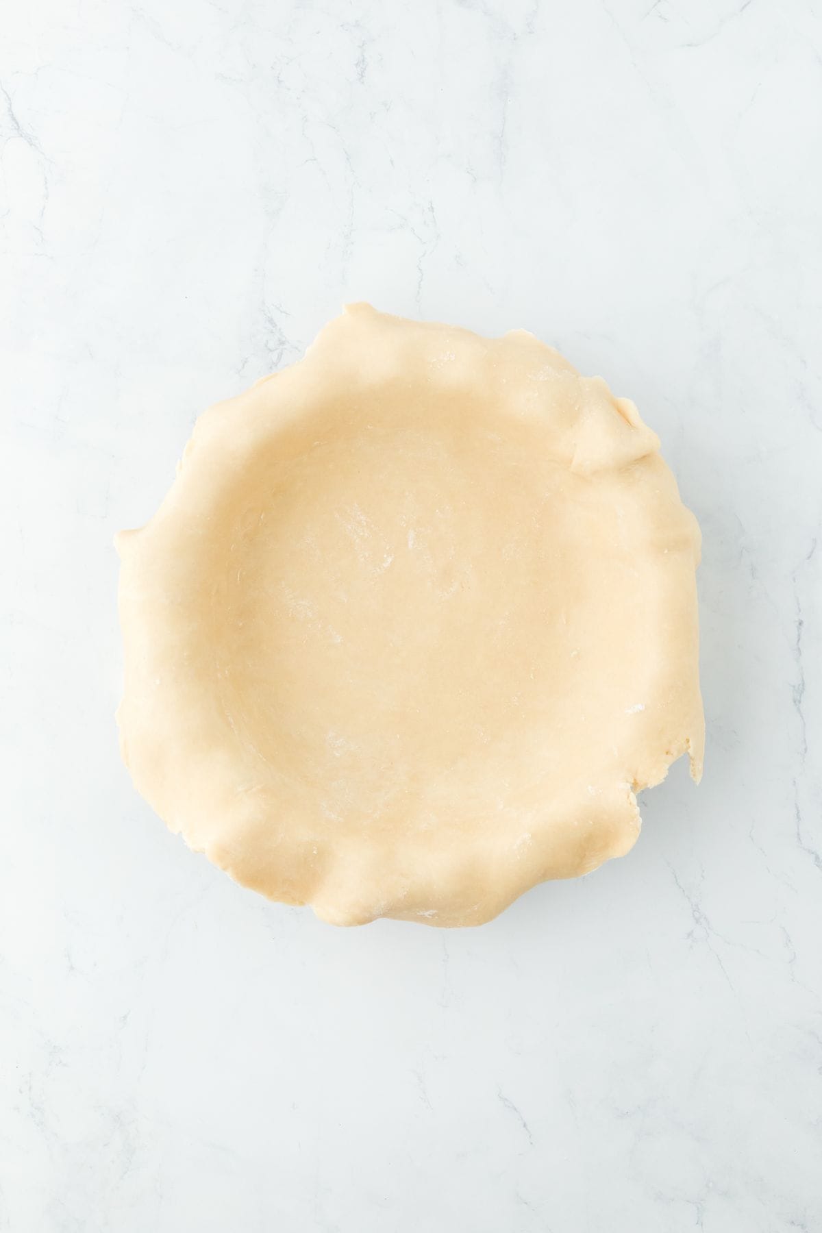 A pie dish with an unbaked pie crust draped over the edges