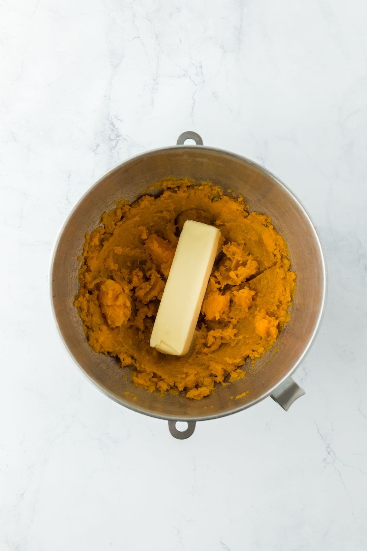 Mashed sweet potatoes in a bowl with a stick of butter on top, ready for mixing