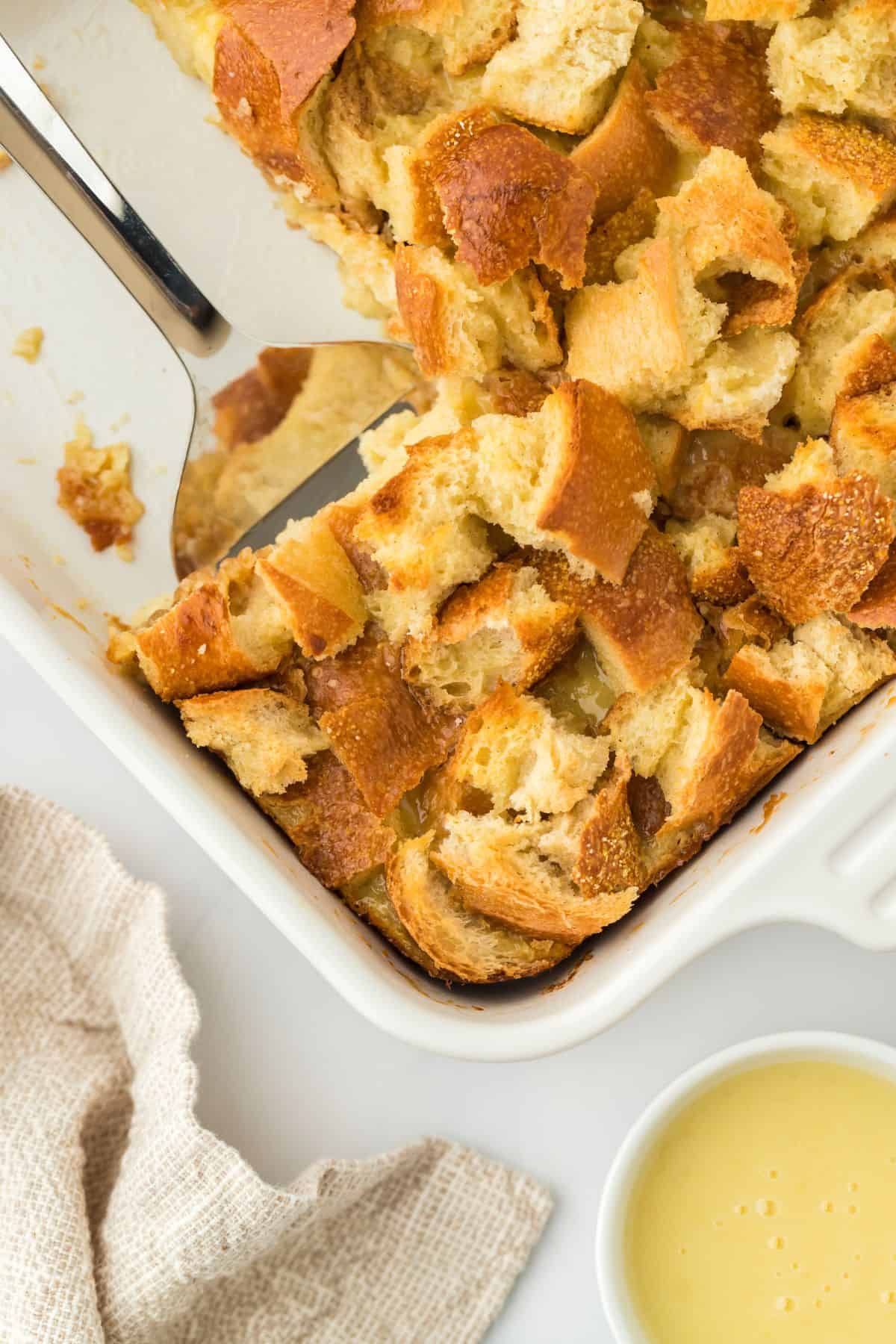 Overhead shot of eggnog bread pudding in a baking dish showing a large portion removed, with a serving spoon resting in the corner