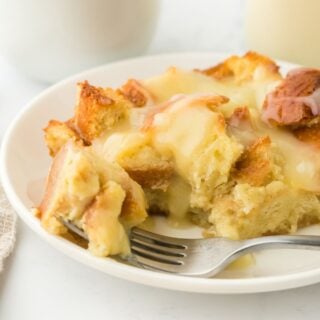 Closeup of eggnog bread pudding with a fork taking a bite and a bowl with vanilla sauce in the background