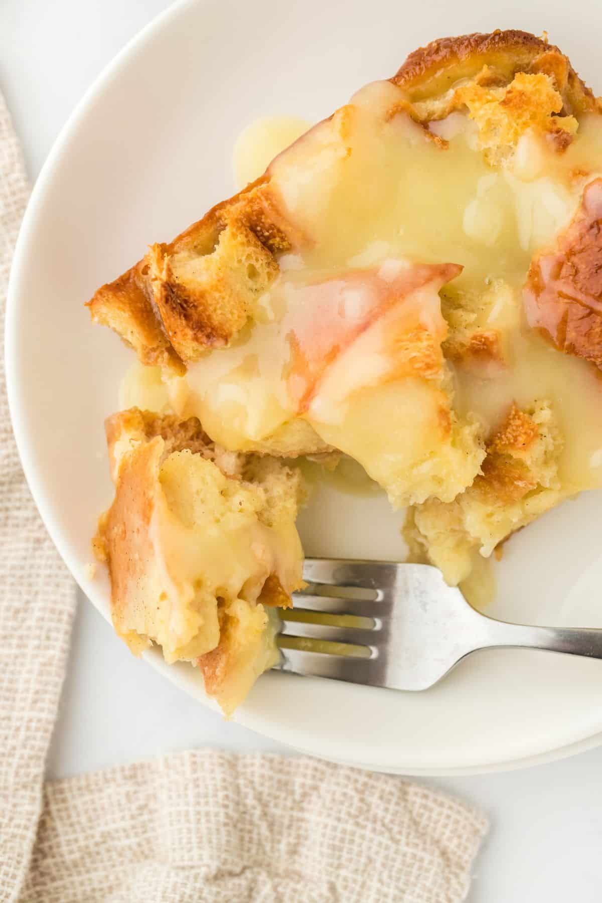 Closeup of a piece of eggnog bread pudding drizzled with vanilla sauce on a white plate with a fork