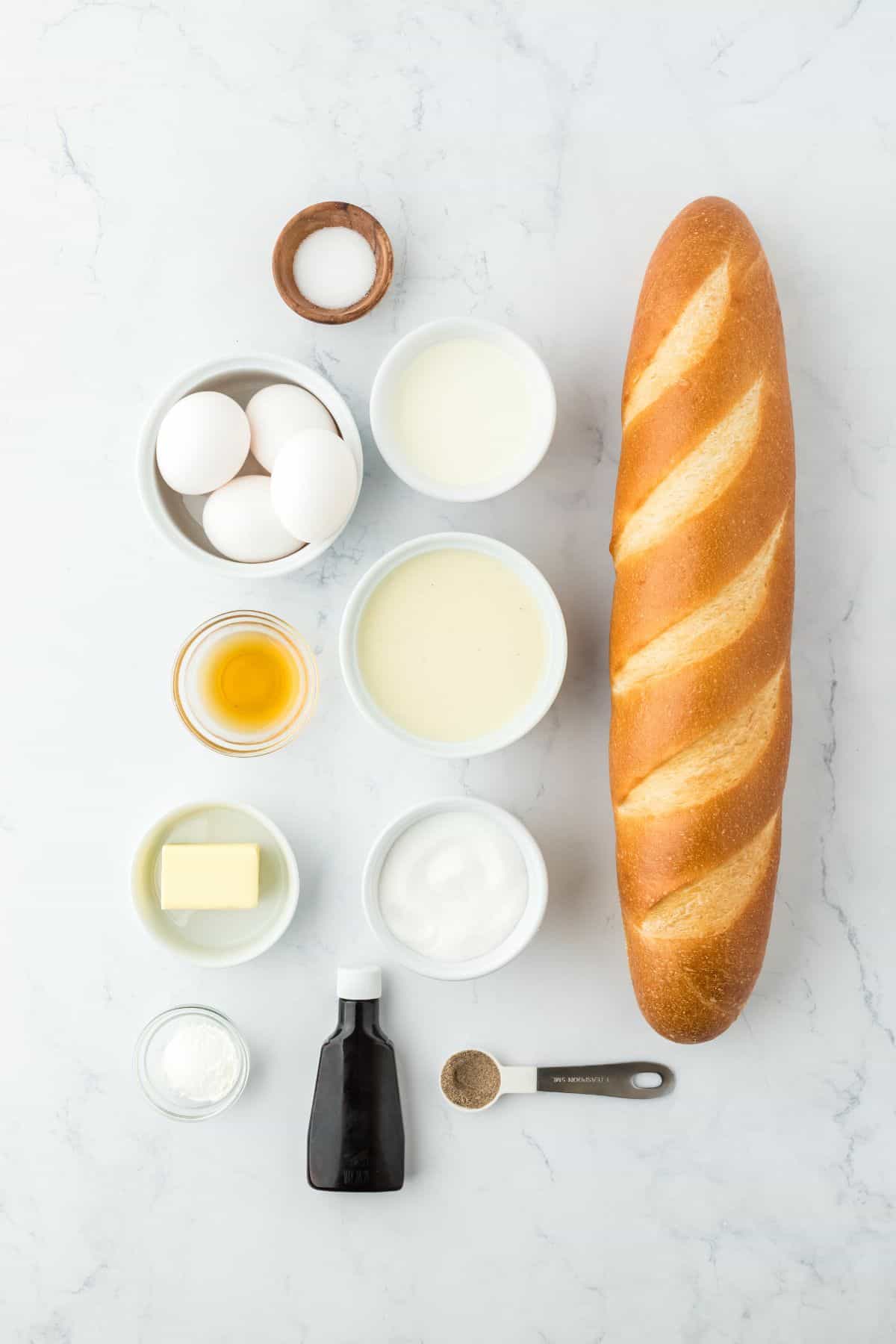 Overhead shot of ingredients to make eggnog bread pudding on a white surface before mixing