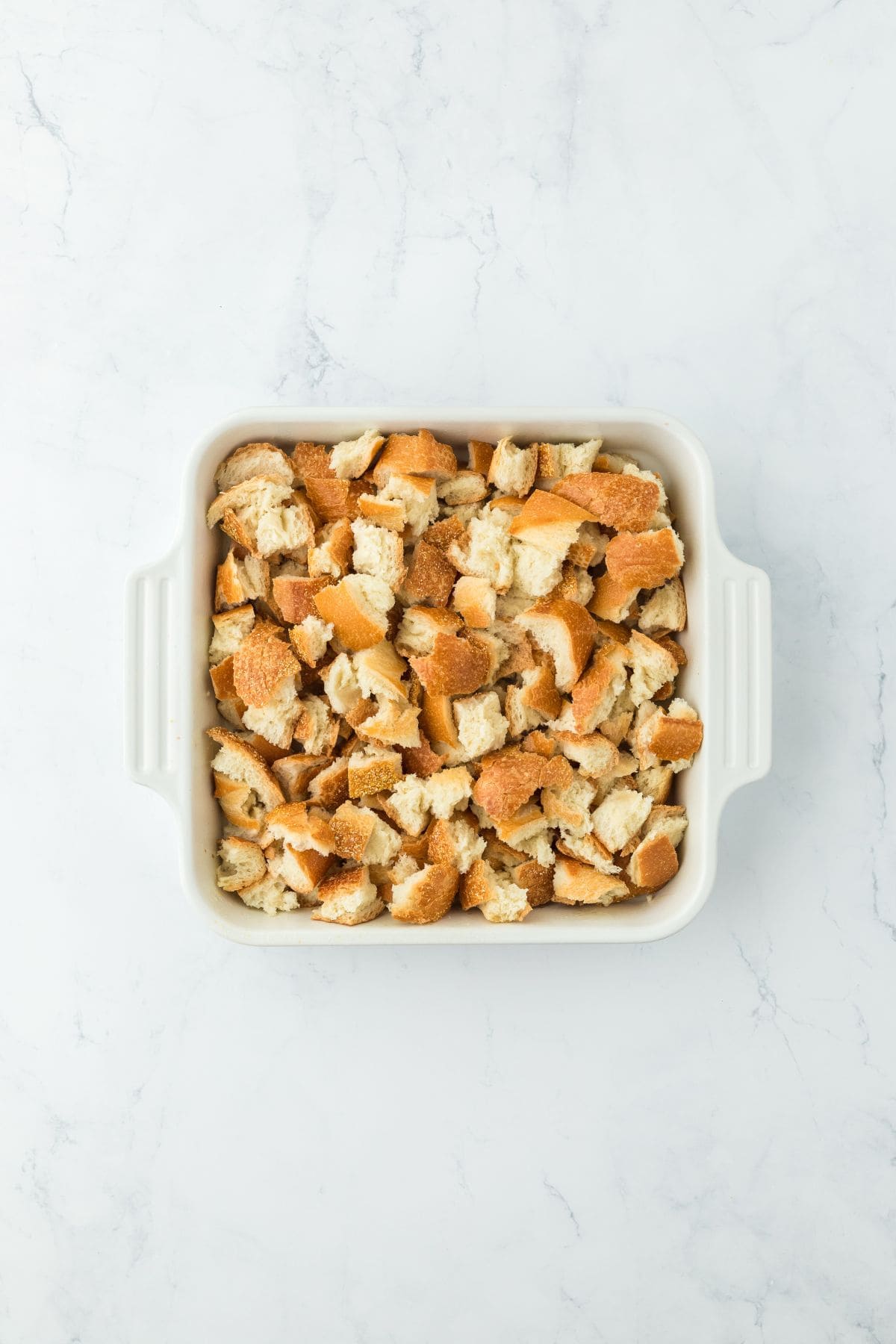 A baking dish filled with torn bread pieces, arranged evenly