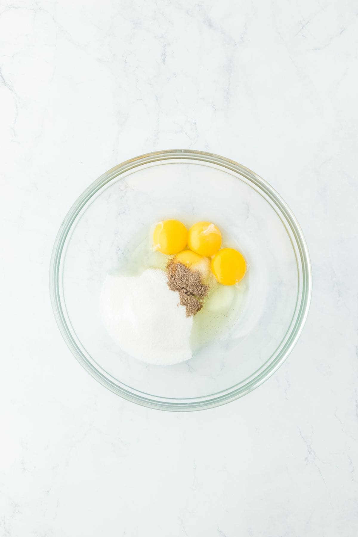 A glass bowl with eggs, sugar, and spices before being mixed