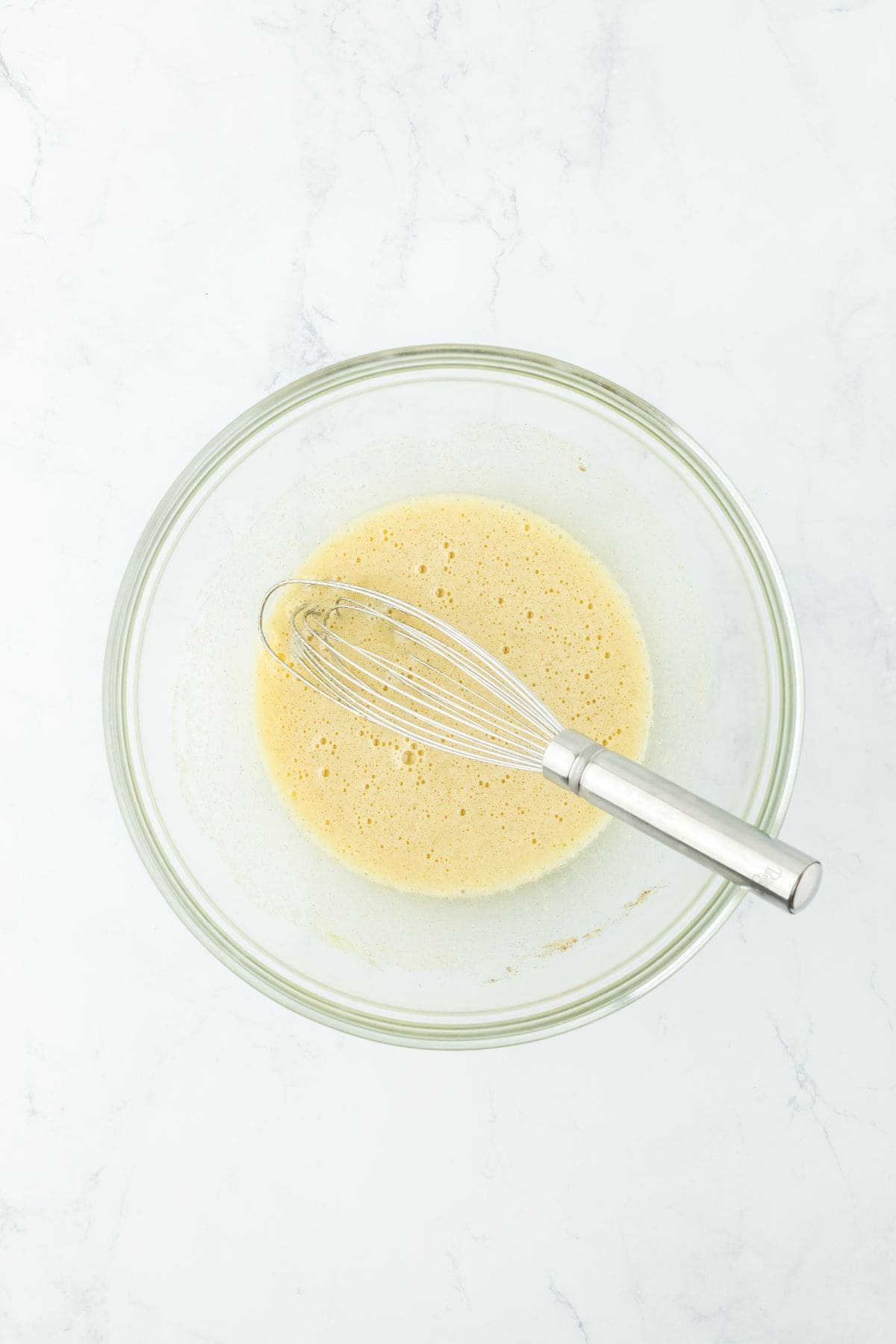 A whisk in a bowl of mixed egg and sugar mixture, frothy and smooth