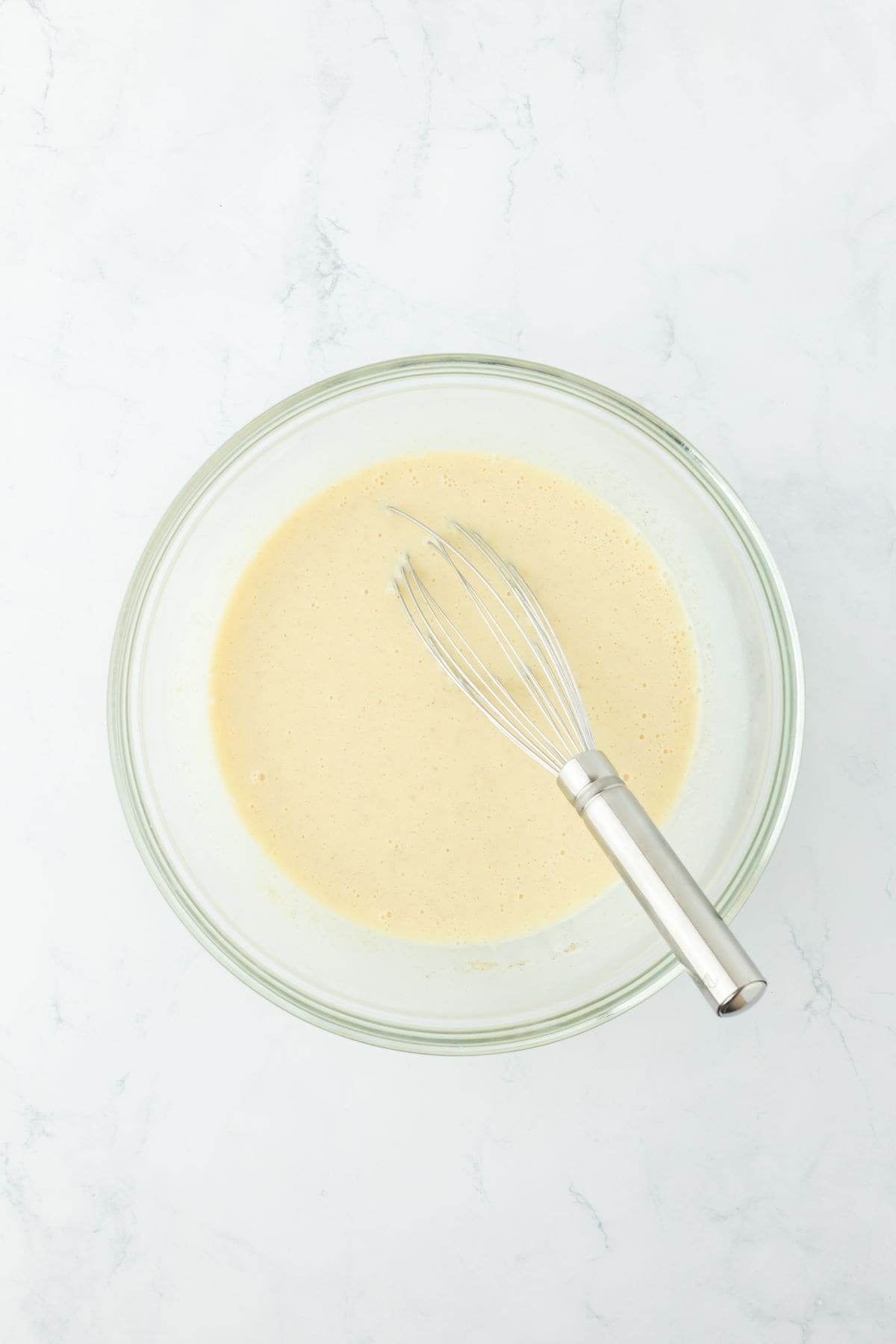 Fully mixed custard in the glass bowl with a whisk resting inside