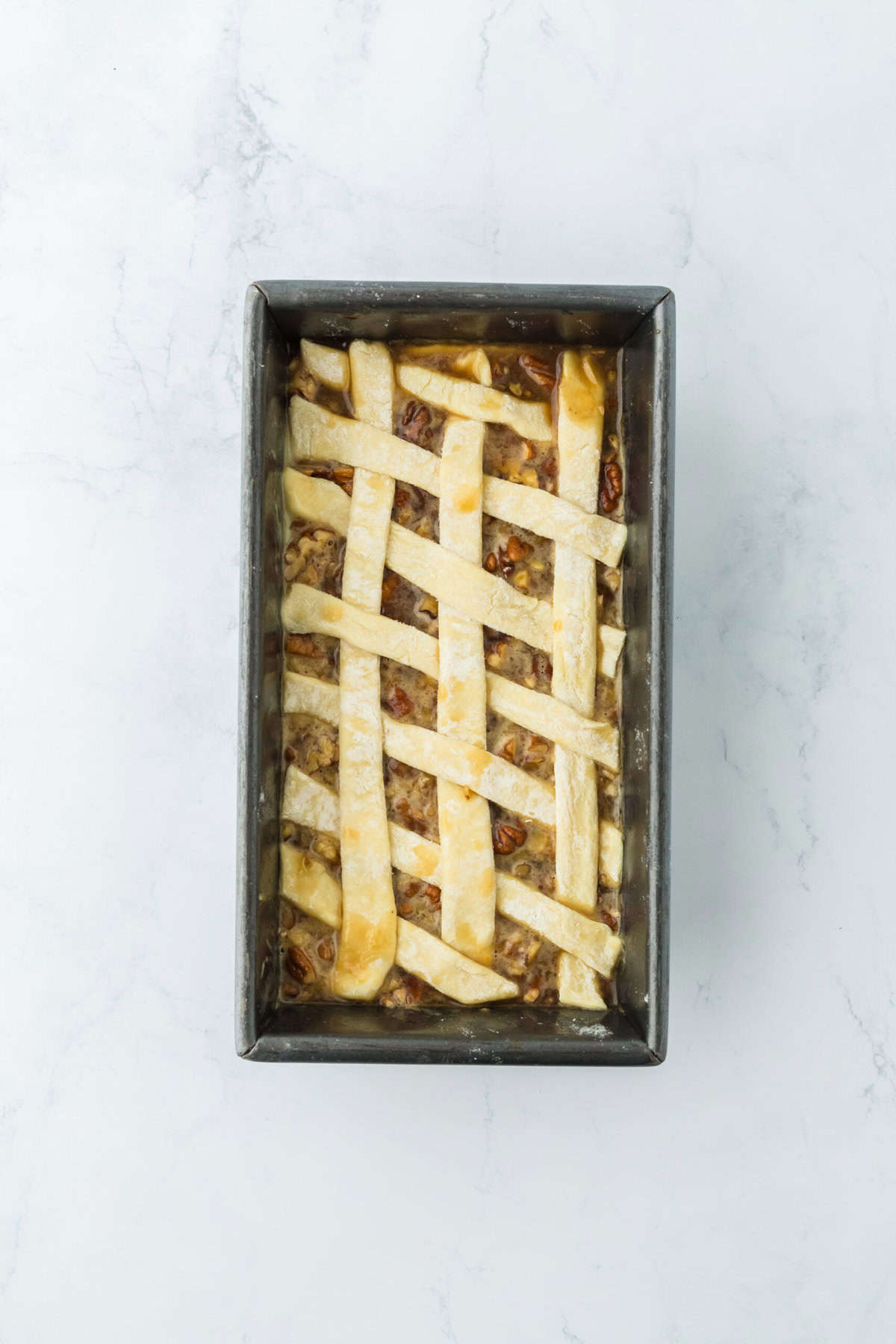 Lattice puff pastry over pecan filling in loaf pan on white countertop.