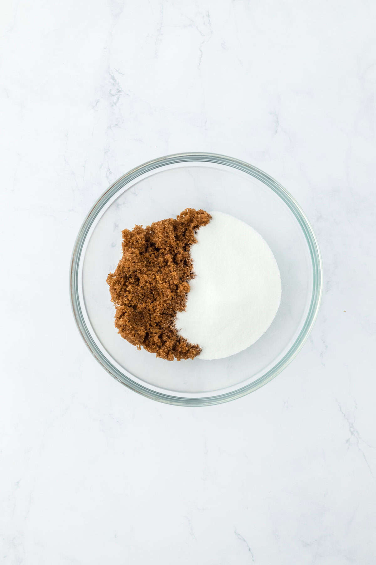 Whisked together brown sugar and granulated sugar in a glass bowl on white countertop