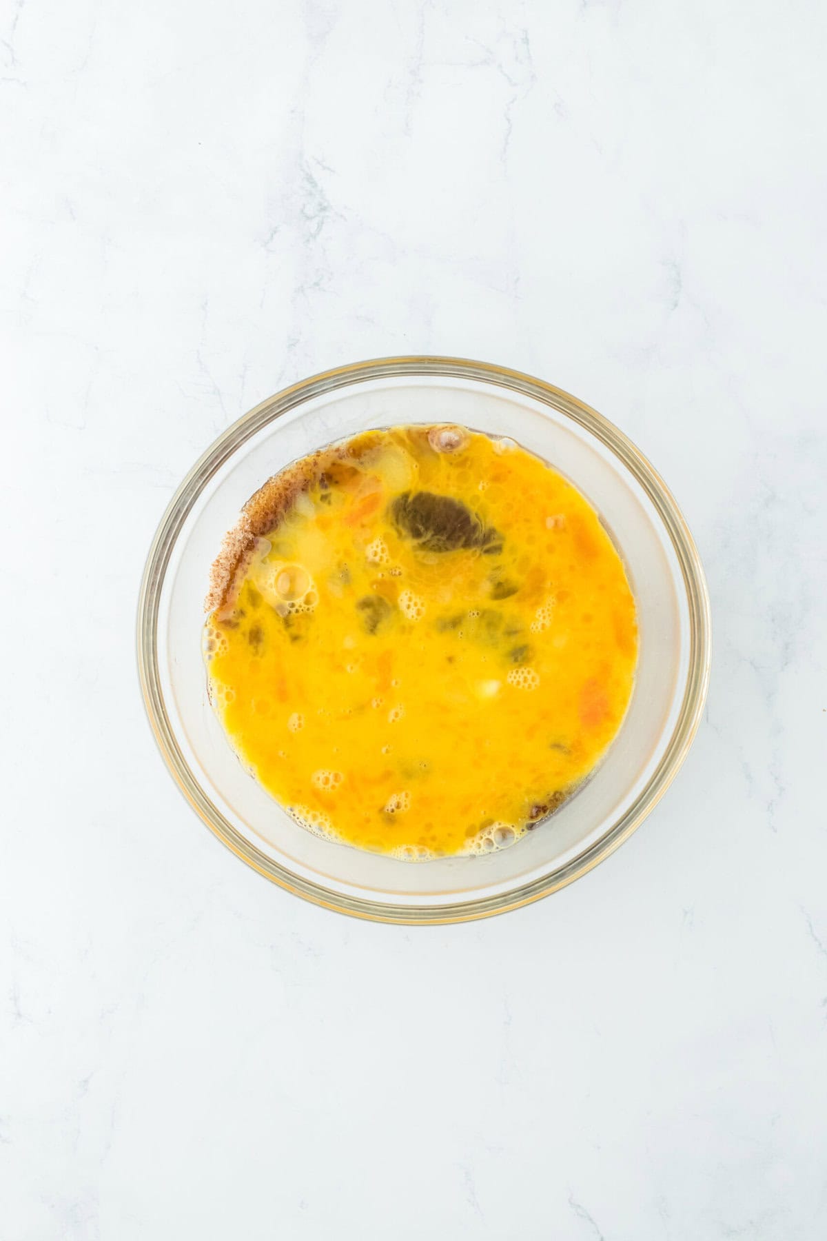 Corn syrup, melted butter, eggs and vanilla in a glass bowl on white countertop