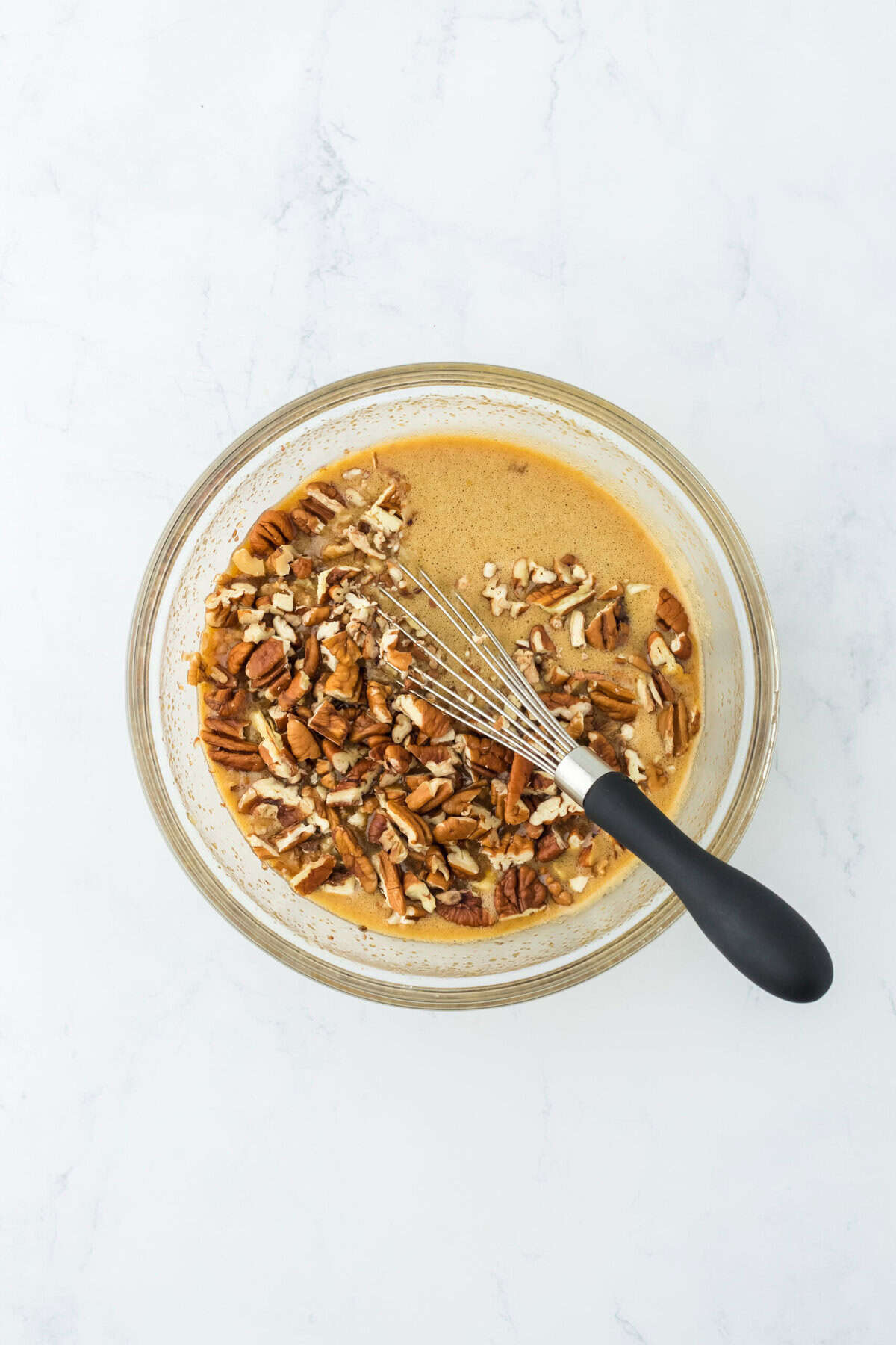 Chopped pecans added to wet gooey filling in glass bowl on white countertop