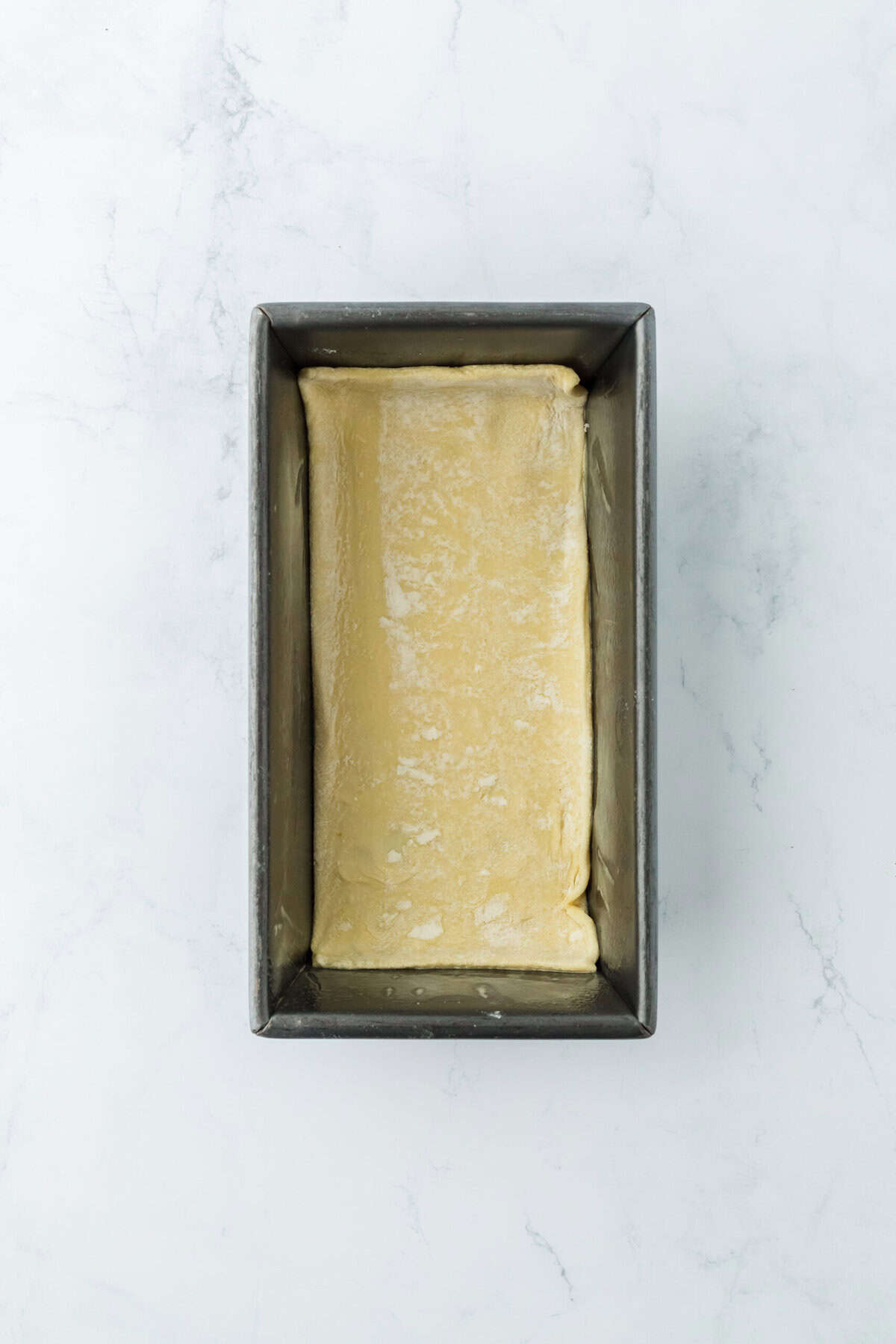 Puff pastry added to a prepared loaf pan on white countertop.