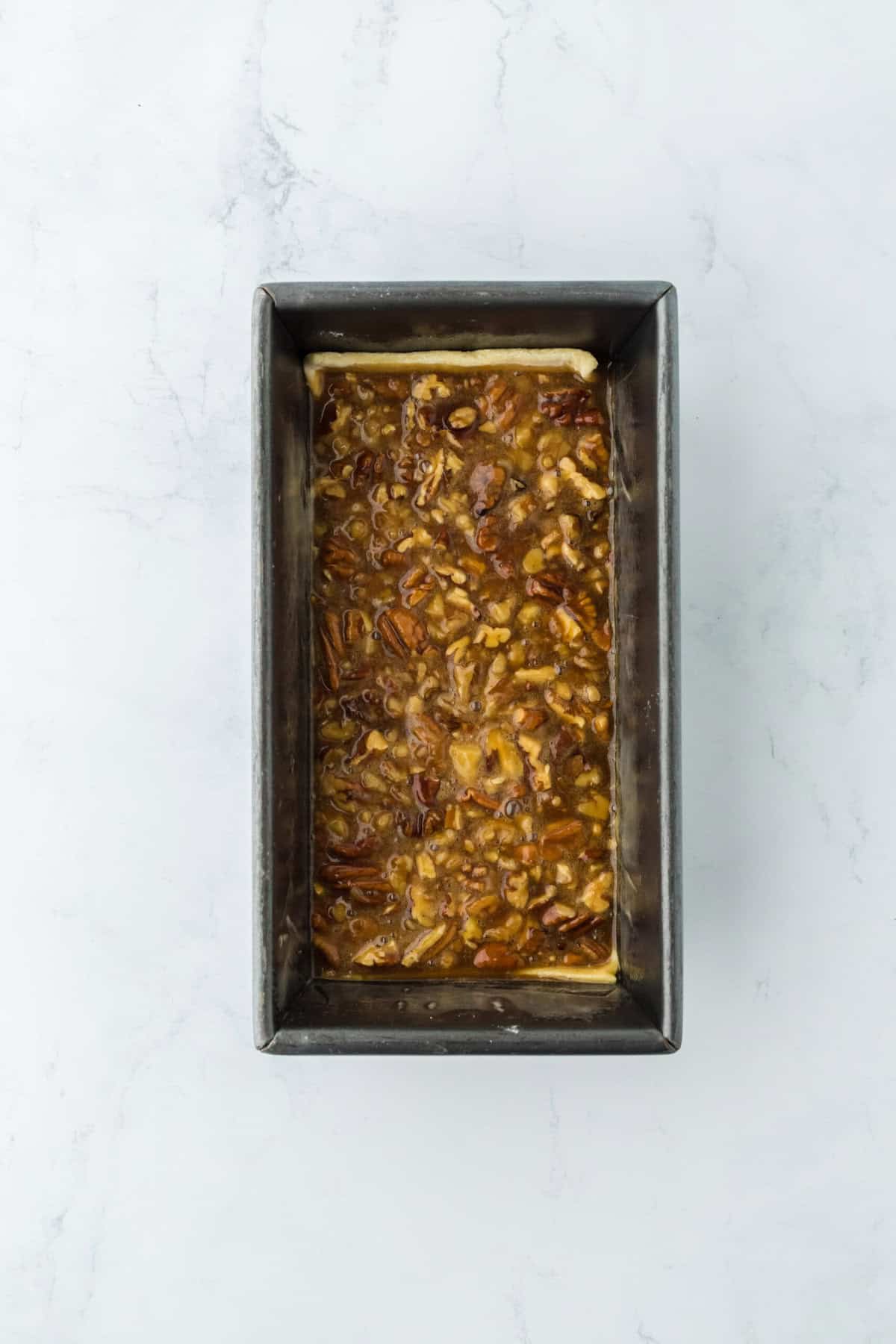 Pecan cobbler filling added to a loaf pan on top of puff pastry on white countertop