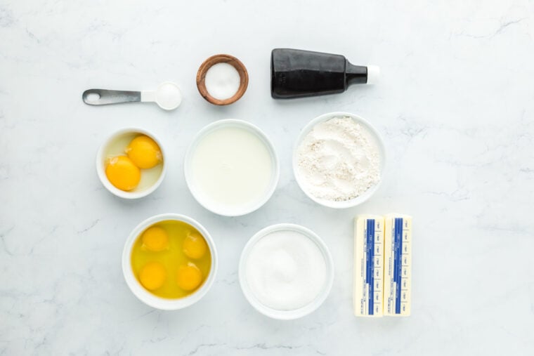 Butter, sugar, eggs, vanilla, flour to make cake recipe in white bowls on white countertop