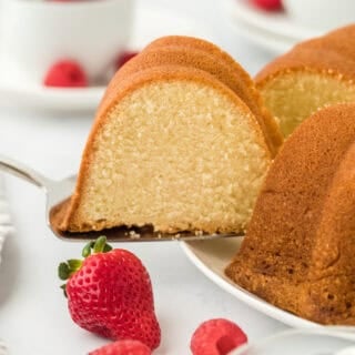 A slice of pound cake being removed to serve with fresh berries and whipped cream