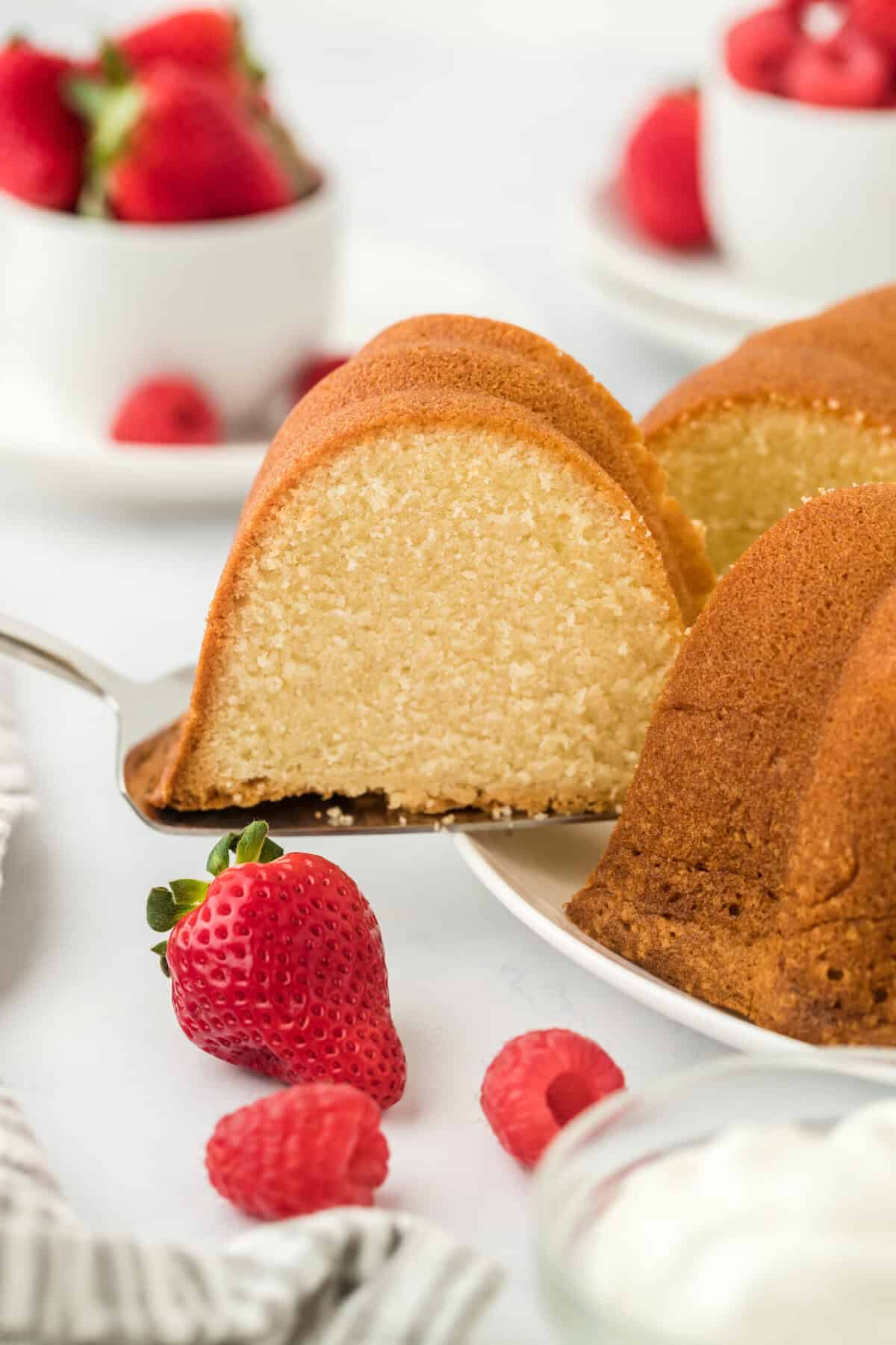 A slice of pound cake being removed to serve with fresh berries and whipped cream