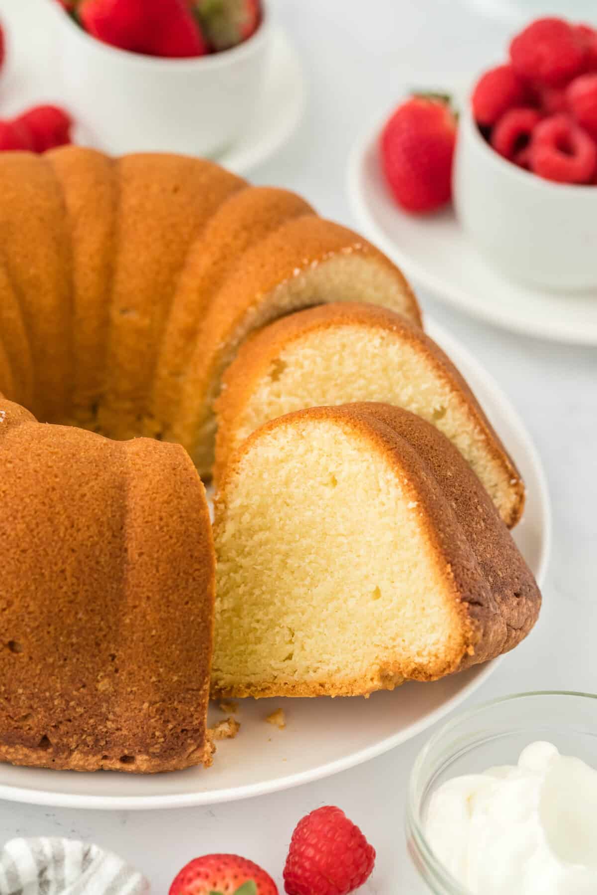 Sliced pound cake recipe on a white plate ready to serve on white countertop with berries and whipped cream