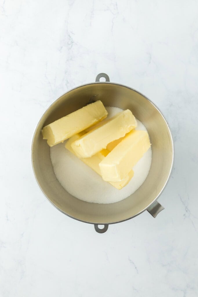 Butter and granulated sugar in a stand mixer bowl on white countertop