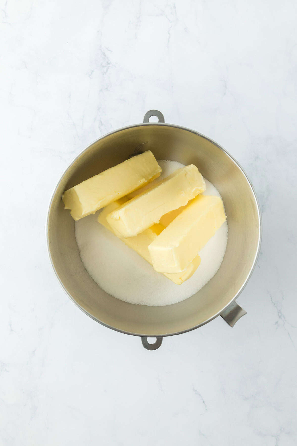 Butter and granulated sugar in a stand mixer bowl on white countertop